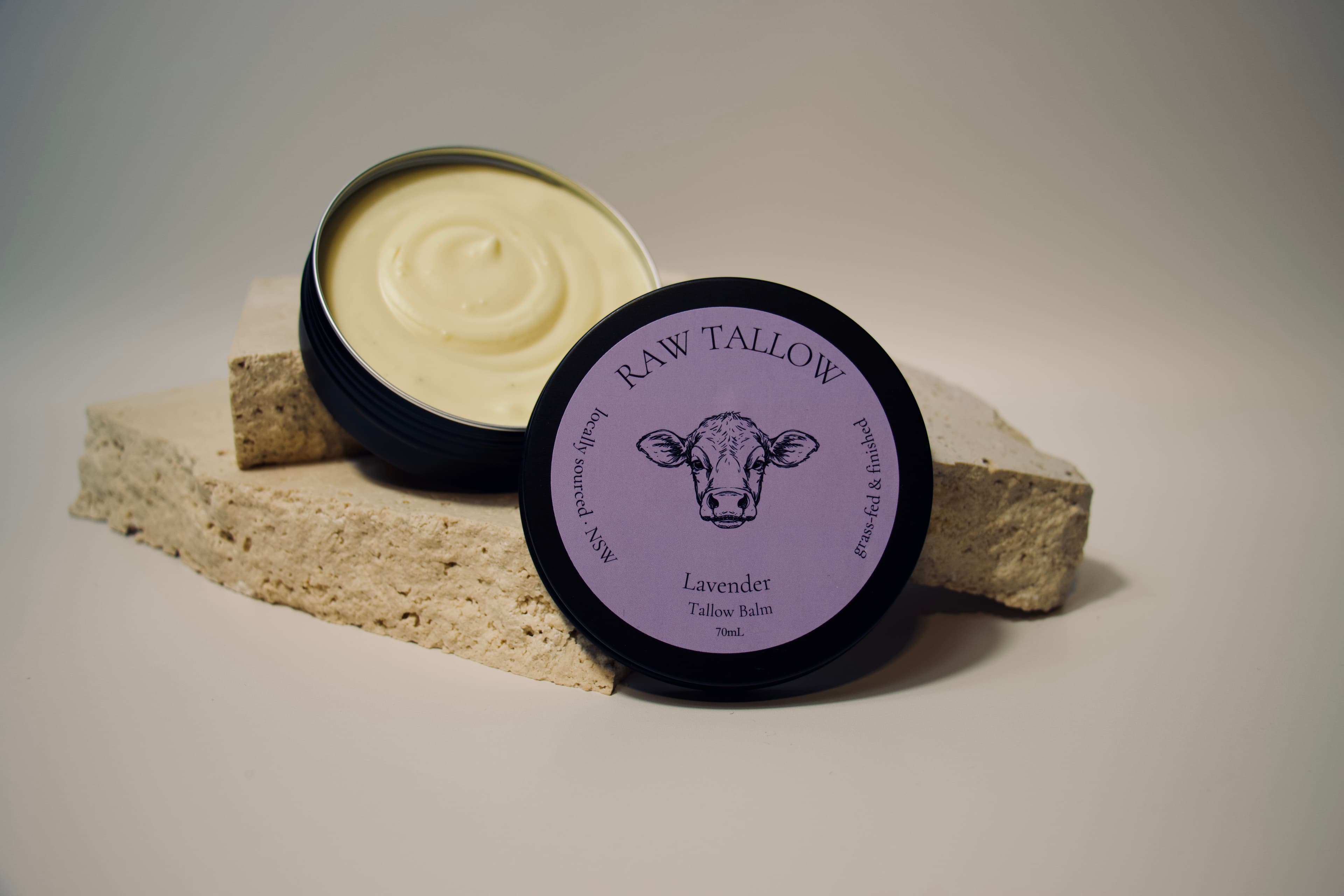 Black amber jar of Raw Tallow Lavender Tallow Balm with purple circular label on travertine stone
