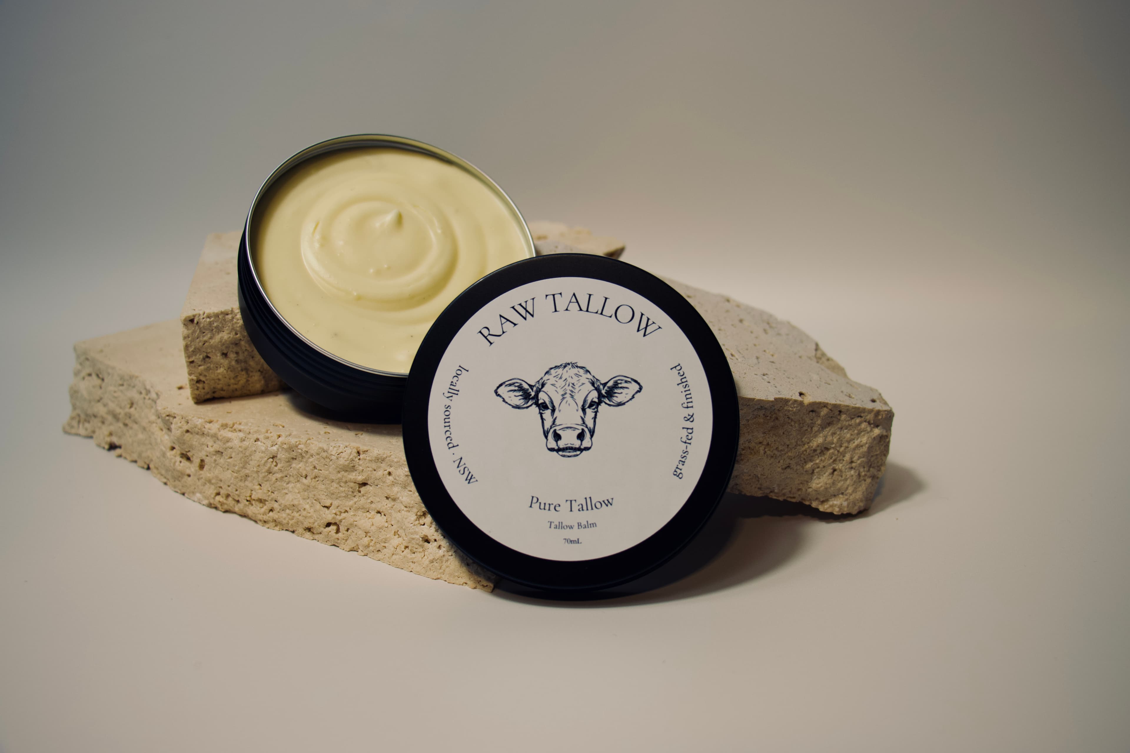Black amber jar of Raw Tallow Pure Tallow Balm with cream-white circular label on travertine stone