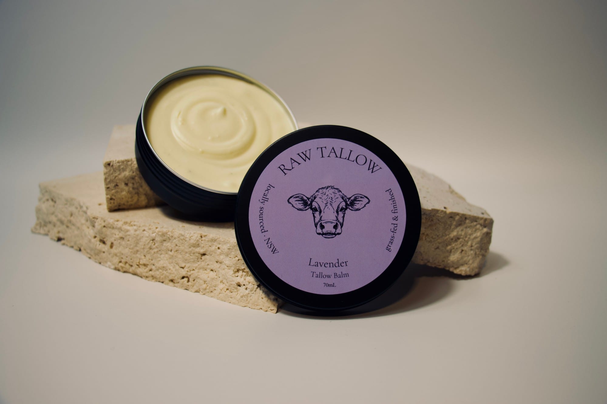 Black amber jar of Raw Tallow Lavender Tallow Balm with purple circular label on travertine stone