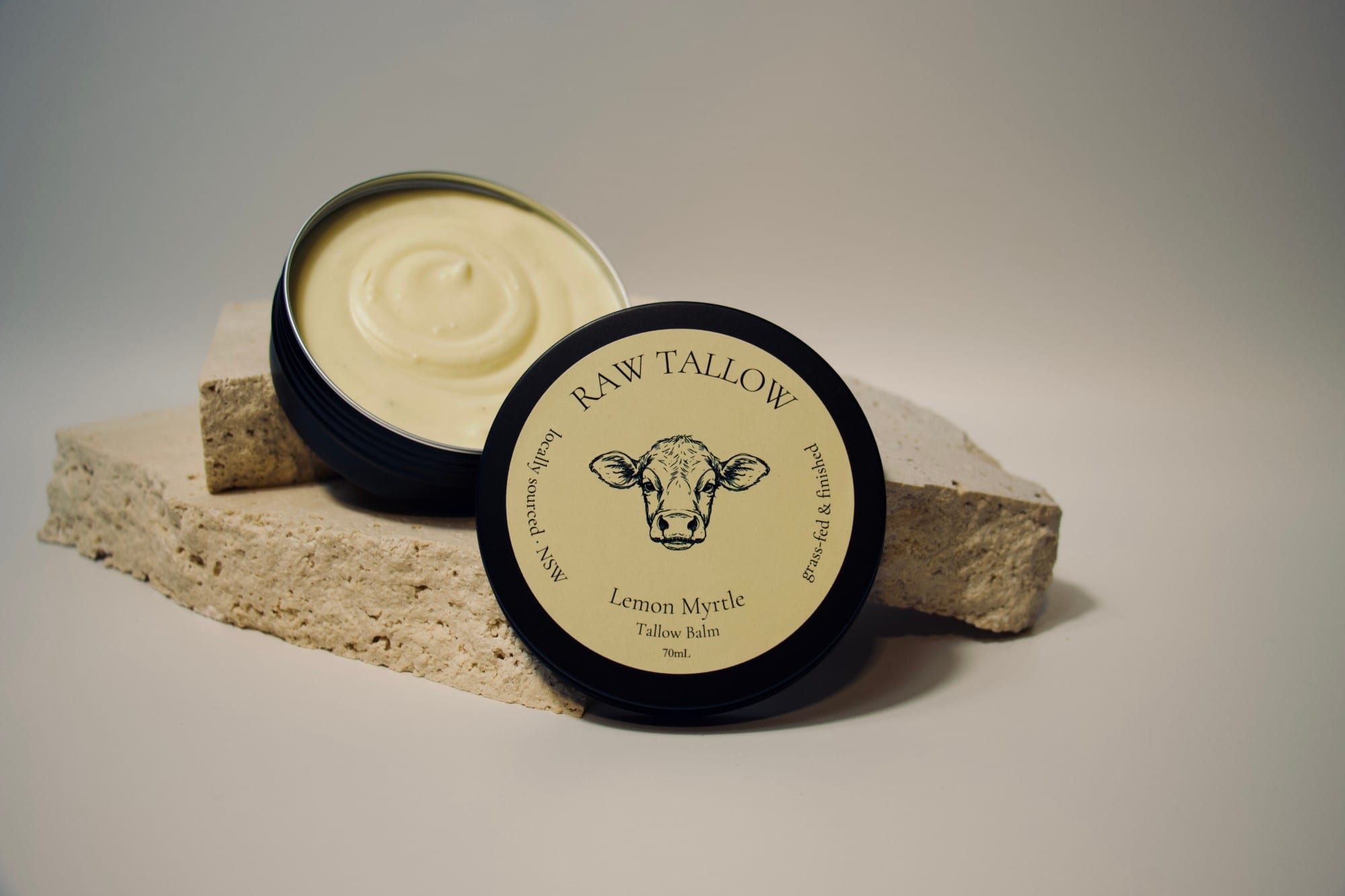 Black amber jar of Raw Tallow Lemon Myrtle Tallow Balm with butter yellow circular label and native myrtle leaves