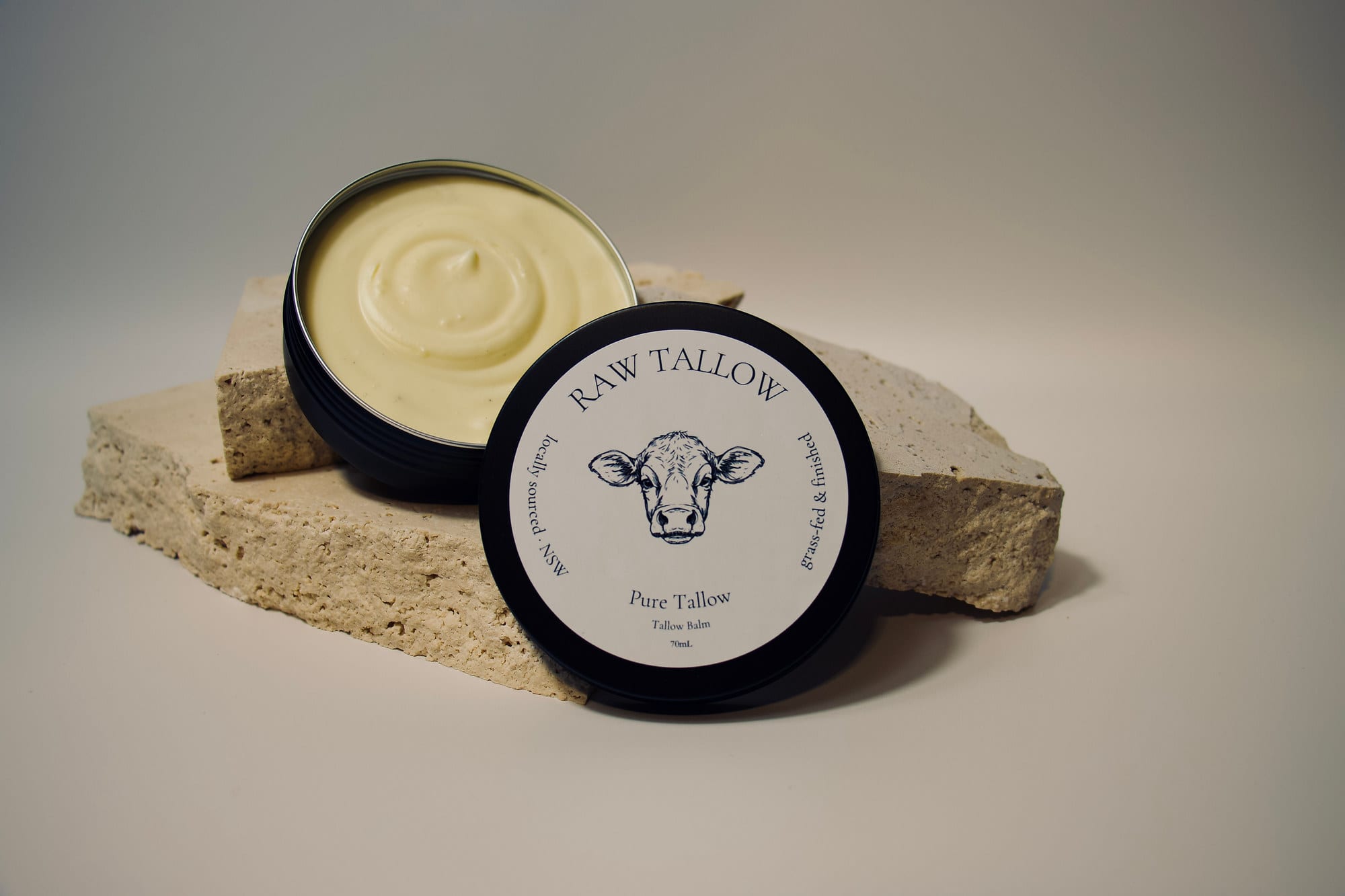 Black amber jar of Raw Tallow Pure Tallow Balm with cream white circular label on travertine stone